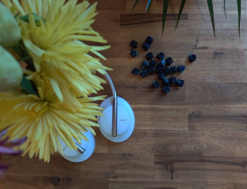 Keyboard switches on a desk next to flowers and headphones.