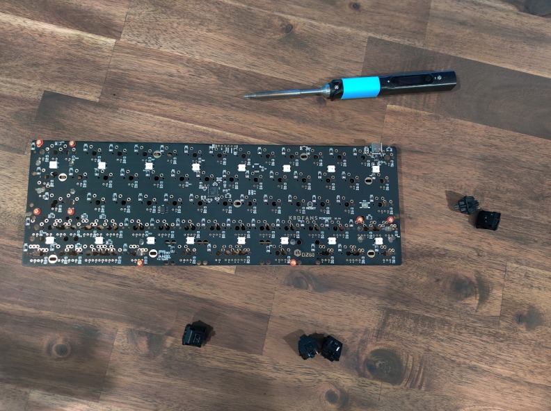 Keyboard PCB on a desk with a soldering iron and keyboard switches.